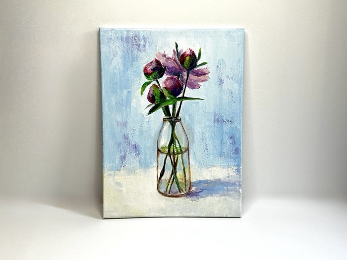 Pink peonies in a clear glass jar against a pale blue background.